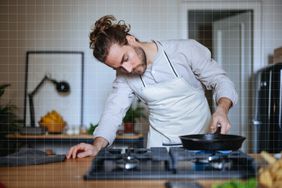a photo of a man looking at his gas stove top while placing his cast iron skillet on top